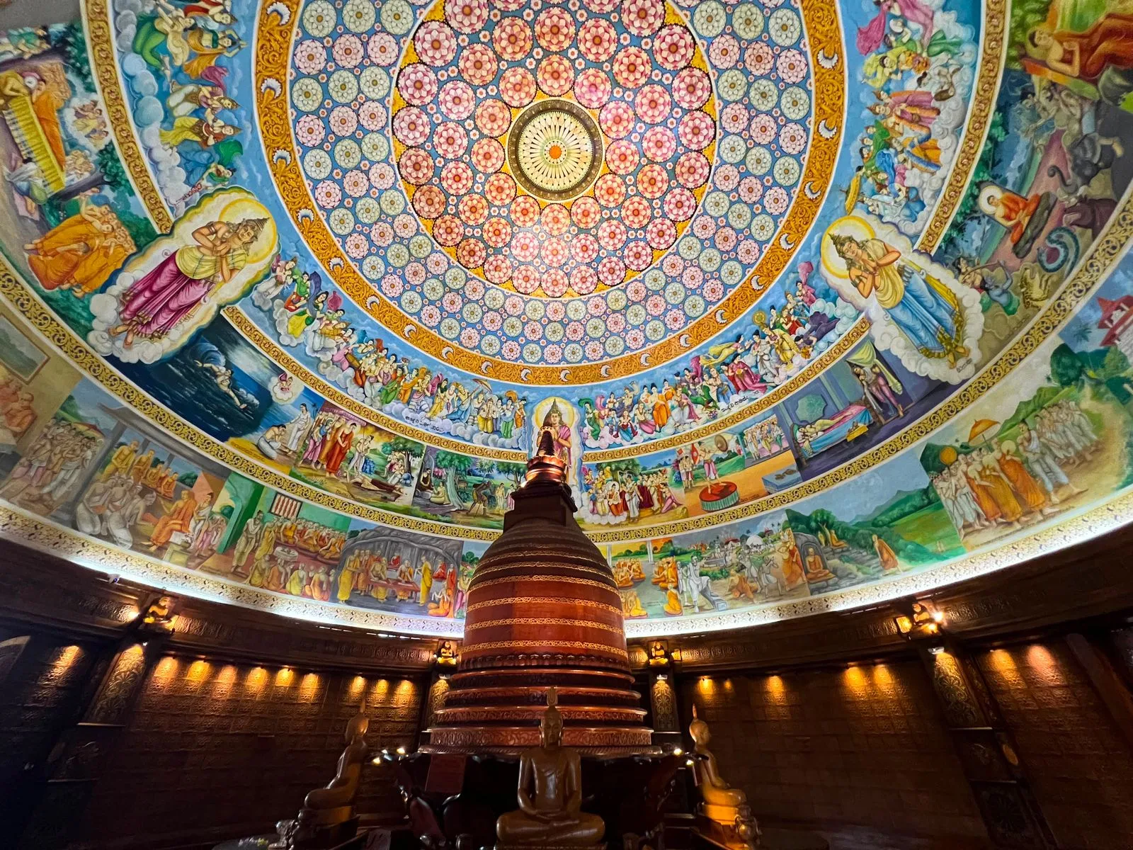 A painted temple dome covered in Buddhist murals above a carved wooden stupa