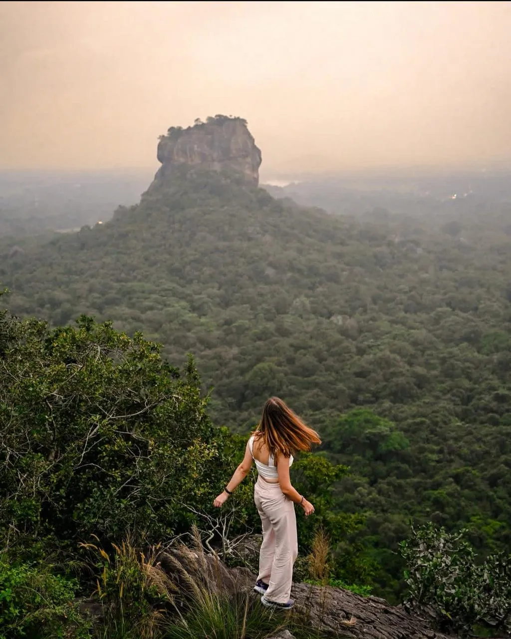 A hiker standing on the rocky edge of Pidurangala looking across the jungle towards Sigiriya at dawn