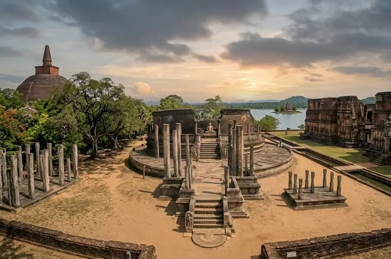 Stone columns and shrines of the Polonnaruwa Quadrangle at sunset, with the Parakrama Samudra reservoir behind