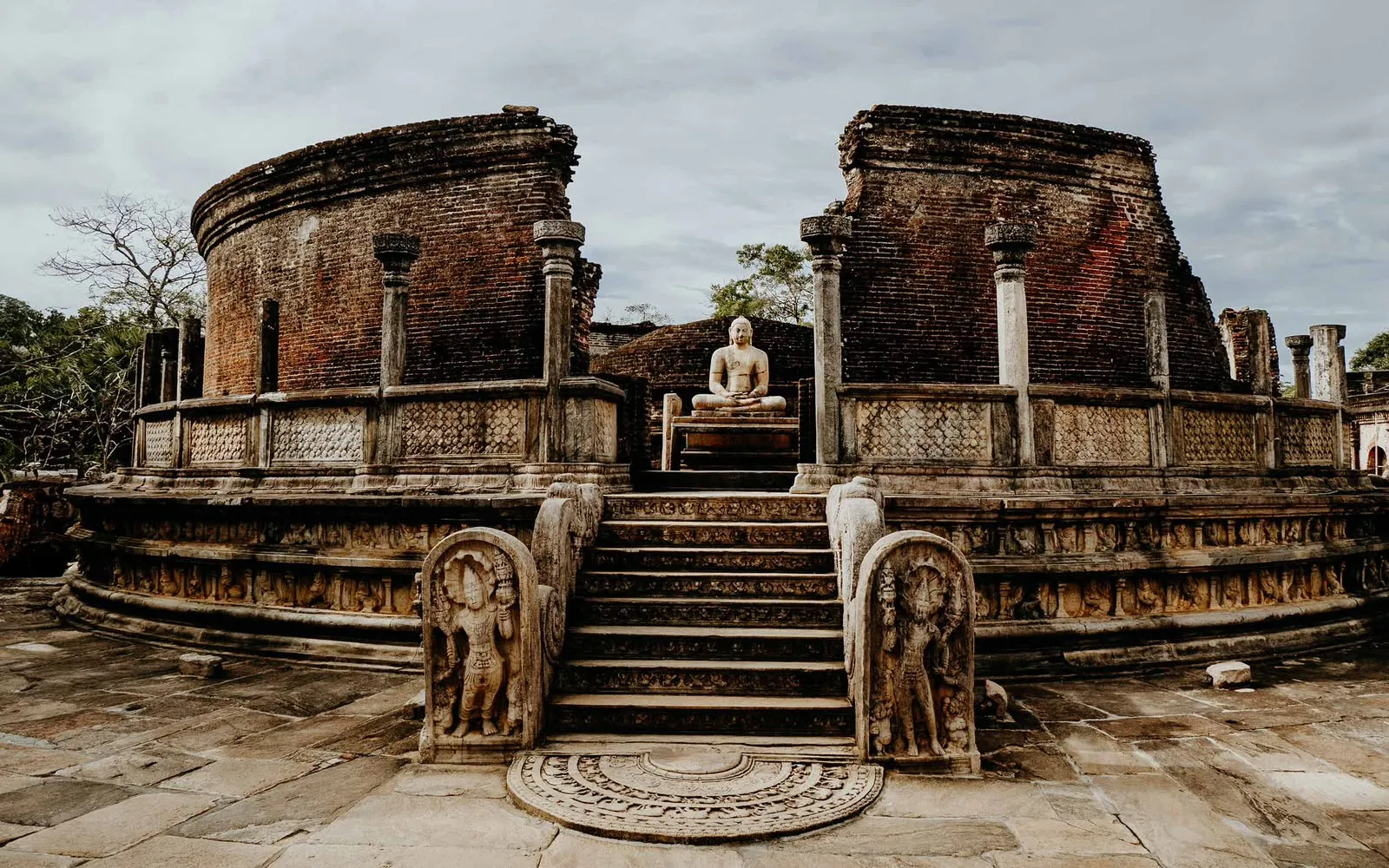 The circular brick Vatadage in Polonnaruwa, with a seated Buddha above carved guardstones and a moonstone at the foot of the stairs