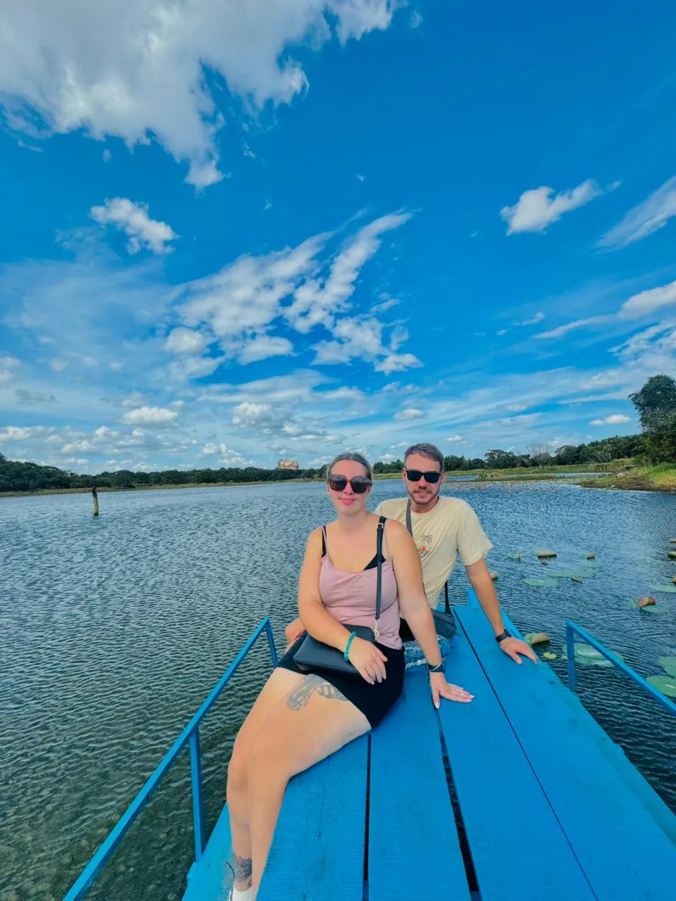 Guests crossing a village tank on a blue catamaran, with Sigiriya rock on the horizon